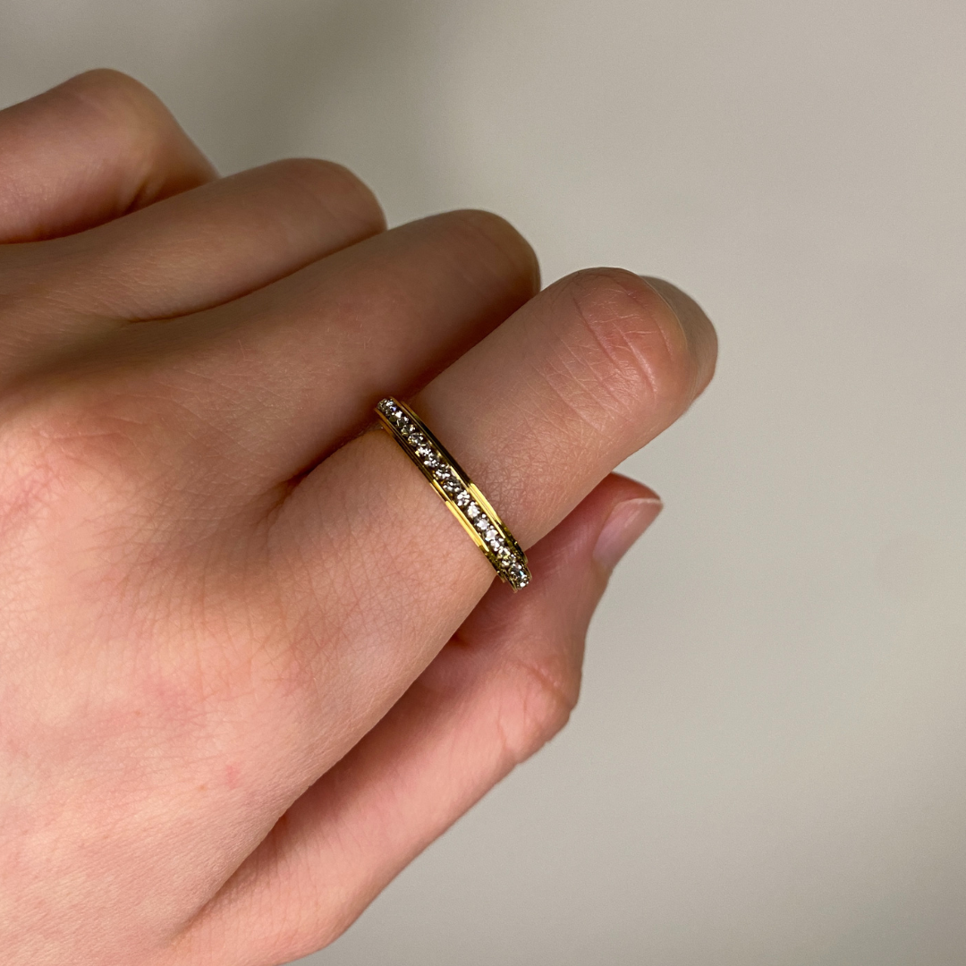 Gold ring with small gemstones on a finger against a neutral background